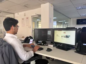 Jeral trabajando en la oficina frente a dos monitores, con código y un sitio web en pantalla